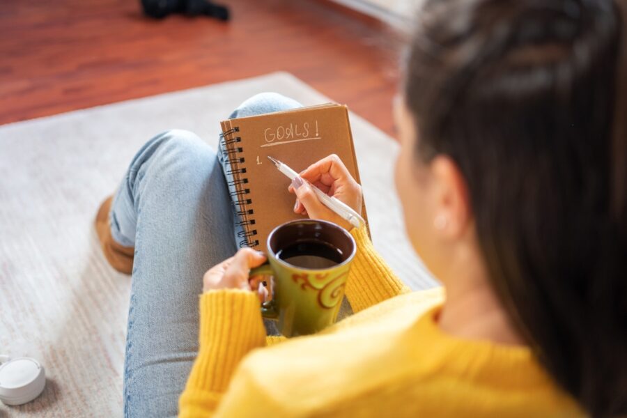 Vrouw schrijft haar doelen op in een notitieboekje.