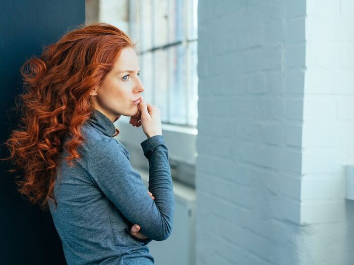Sad lonely thoughtful young woman with gorgeous long curly red hair standing sideways indoors staring though a window|Sad lonely thoughtful young woman with gorgeous long curly red hair standing sideways indoors staring though a window