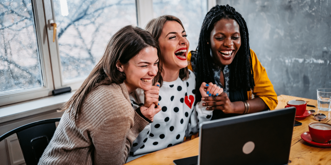 drie schaterlachende vrouwen achter een laptop