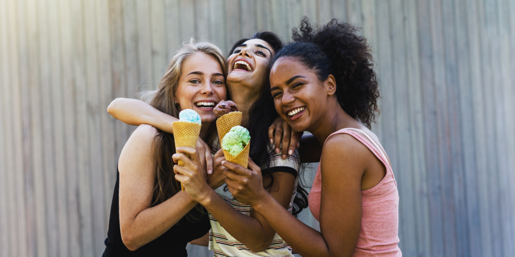 drie vrolijke vrouwen knuffelen elkaar en eten een ijsje|drie vriendinnen aan tafel