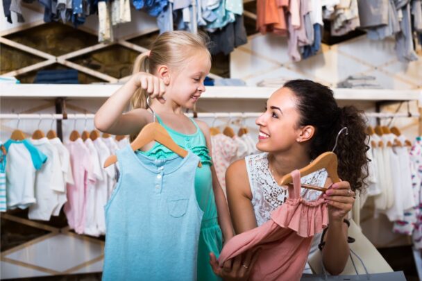 Klein meisje is met haar moeder in een kinderkledingwinkel. Samen bekijken ze kleding.