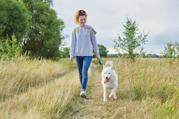 Vrouw laat hond uit in een bosrijk heidegebied.