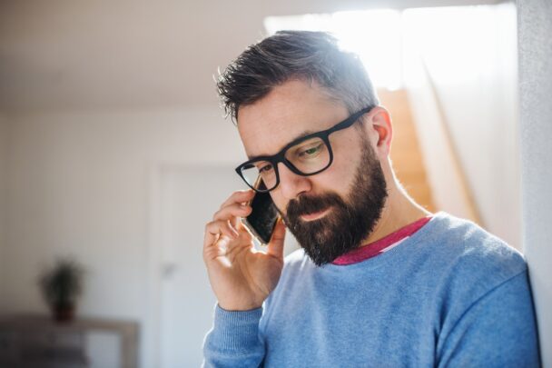 Man met blauwe trui en bril voert een telefoongesprek.