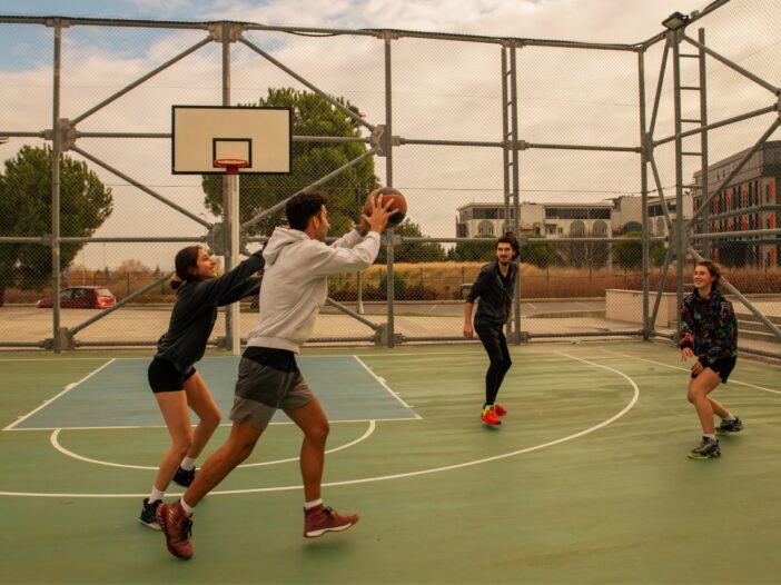 Vier jongeren spelen basketbal in een park.