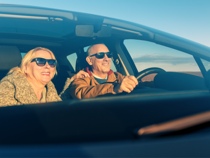 Twee lachende mensen in een auto samen. De zon schijnt en de man is de chauffeur van de vrouw.