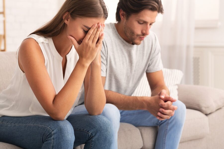 Vrouw en man zitten samen op de bank. De vrouw is verdrietig.