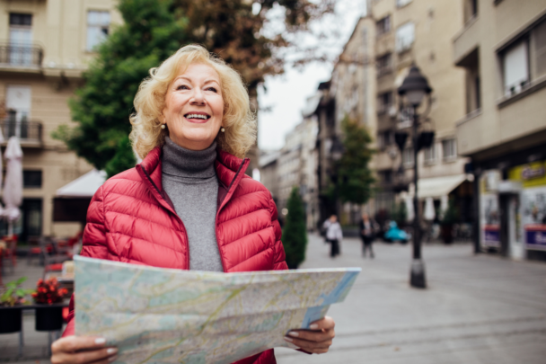 vrouw met rode bodywarmer loopt met een glimlach op haar gezicht door een stad. In haar handen heeft ze een kaart.