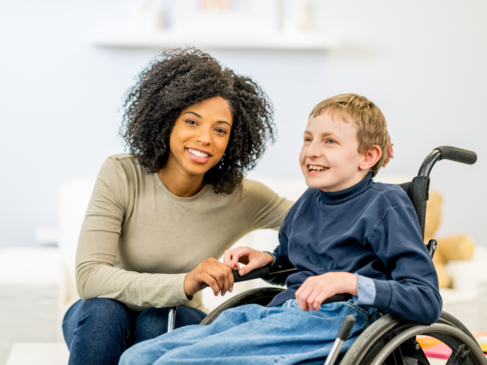 Vrouw helpt jongetje in rolstoel. De vrouw is heeft krullen en ze lachen allebei.