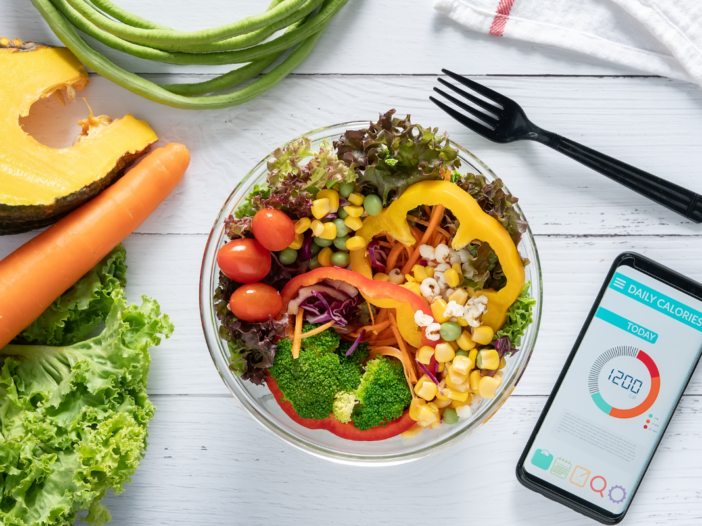 Een schaal met kleurrijke groentes op tafel. En een telefoon met een meet app.