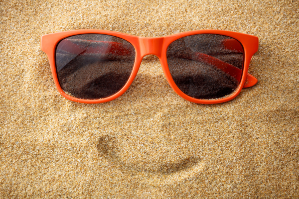 Oranje zonnebril op het strand met een getekende glimlach er onder