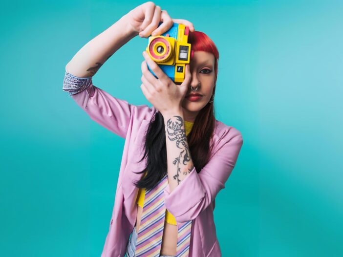 Vrouw met rood haar in een kleurrijke outfit maakt een foto richting de kijker