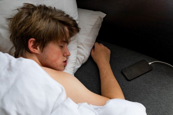 Dit is een jongen die met zijn telefoon in bed slaapt. Hij heeft zijn telefoon aan de oplader liggen in zijn bed.