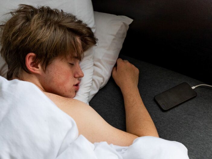 Dit is een jongen die met zijn telefoon in bed slaapt. Hij heeft zijn telefoon aan de oplader liggen in zijn bed.