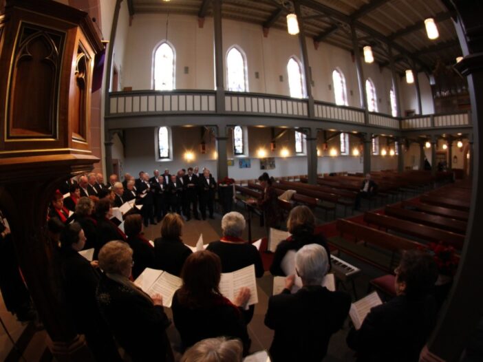 Ze zitten met z'n alle in een kerk te zingen. Ze hebben allemaal muziekbladen in hun handen.