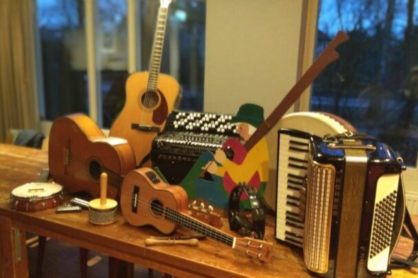 Muziekinstrumenten op tafel. Zoals een gitaar, ukelele, accordeon en een banjo. Deze instrumenten kun je allemaal vinden bij de volksmuziekmiddag in son en breugel.