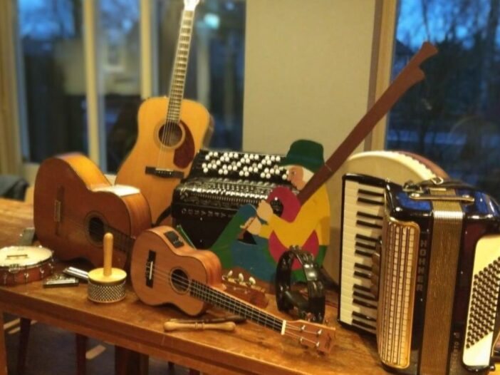 Muziekinstrumenten op tafel. Zoals een gitaar, ukelele, accordeon en een banjo. Deze instrumenten kun je allemaal vinden bij de volksmuziekmiddag in son en breugel.