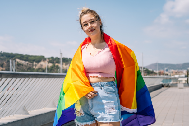 Jonge vrouw met een pride vlag over haar schouders geslagen