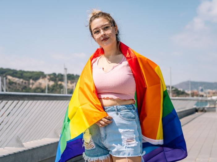 Jonge vrouw met een pride vlag over haar schouders geslagen