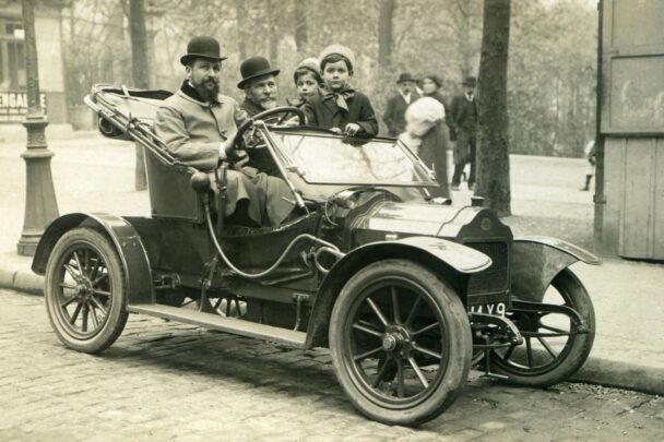 Een foto met een oude look. Van een open oude auto met inzittenden.