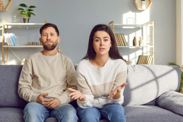 Man en vrouw zitten samen op de bank en kijken moedeloos in de camera