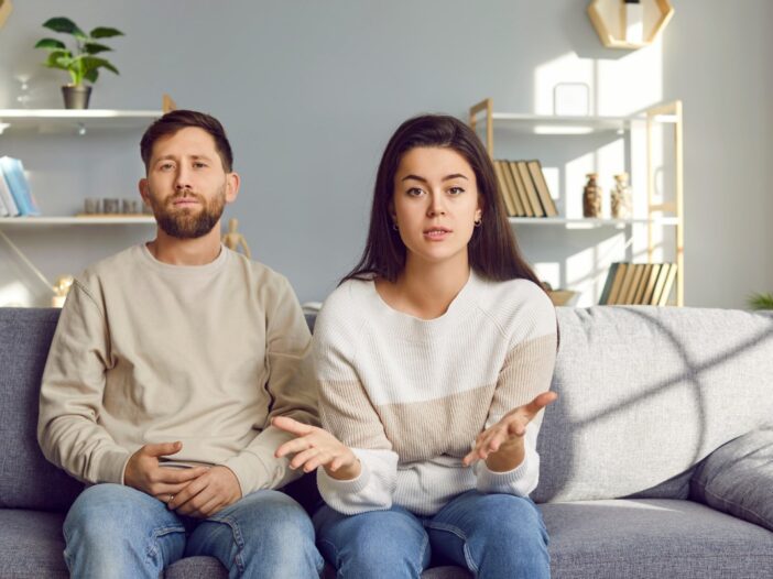 Man en vrouw zitten samen op de bank en kijken moedeloos in de camera