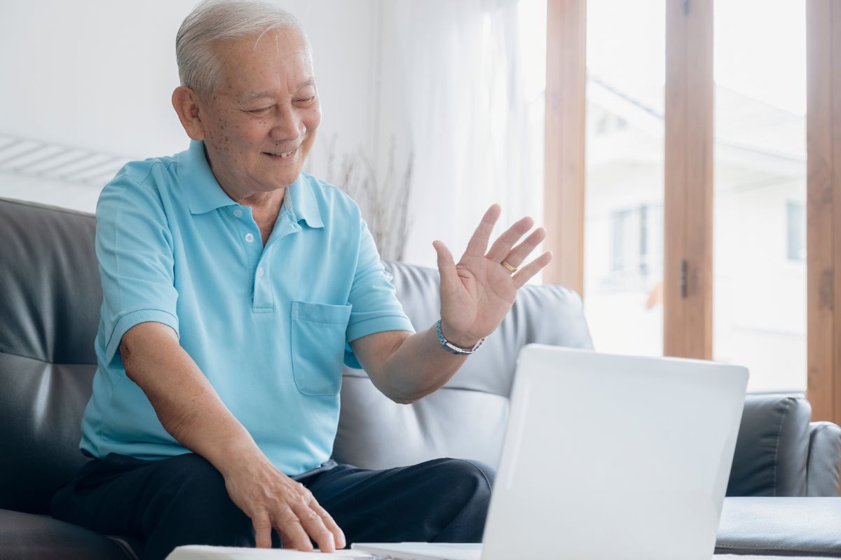 Oudere man is aan het beeldbellen via een laptop, hij zwaait