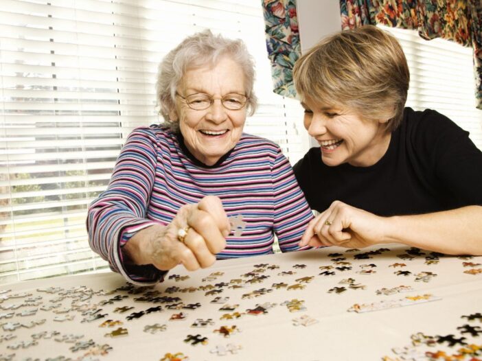 Een oudere vrouw legt samen met een jonge vrouw een puzzel