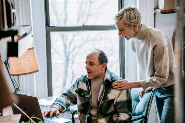 Vrouw en man kijken samen naar computerscherm, de vrouw lacht