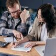 Man en vrouw doen samen de administratie. Op tafel ligt een rekenmachine, papieren en een laptop.