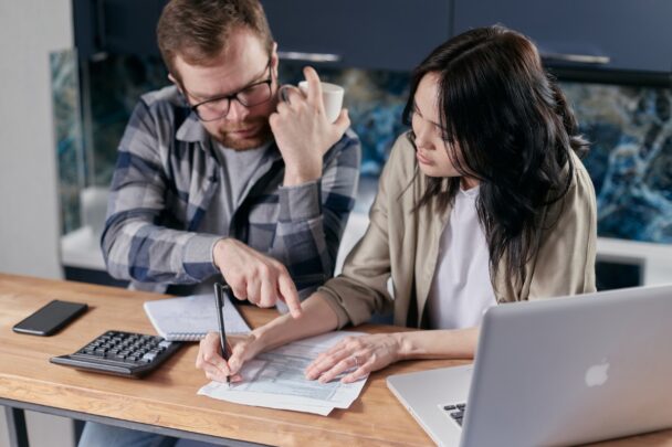 Man en vrouw doen samen de administratie. Op tafel ligt een rekenmachine, papieren en een laptop.