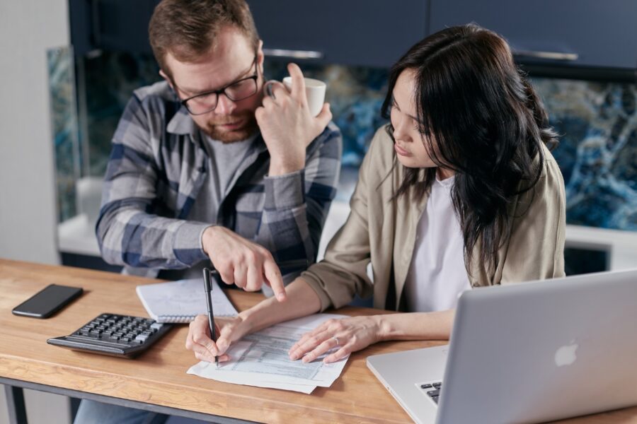 Man en vrouw doen samen de administratie. Op tafel ligt een rekenmachine, papieren en een laptop.