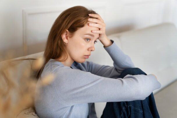 Vrouw zit gespannen op de bank en kijkt angstig.