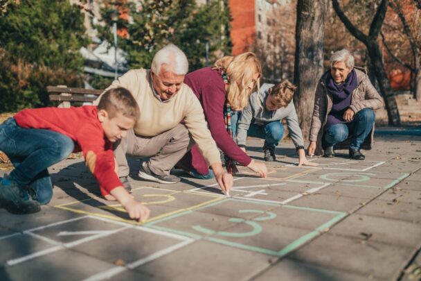 Twee ouderen zijn buiten aan het stoepkrijten met twee kinderen en een jonge vrouw