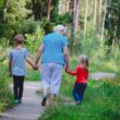 Oudere vrouw maakt met twee kleine kinderen een wandeling in een groene omgeving.