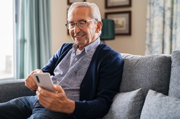 Oudere man zit met smartphone op de bank.