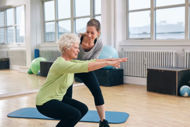 Oudere vrouw traint samen met een jongere vrouwelijke coach in een sportzaal.