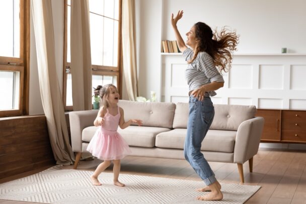 Een vrouw danst met haar dochter in hun woonkamer. Het meisje draagt een roze tutu