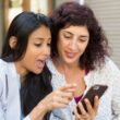 Twee jonge vrouwen kijken samen naar een smartphone en lijken onder de indruk van iets wat ze daar op zien