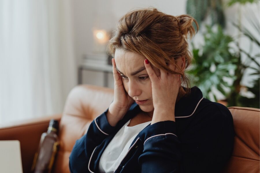 Vrouw zit met haar handen aan haar hoofd op de bank. Ze oogt gestresst.