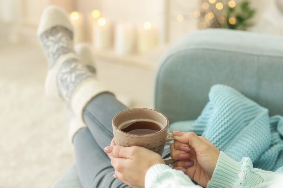 Vrouw zit ontspannen op de bank met een kopje thee en zachte huissokken aan