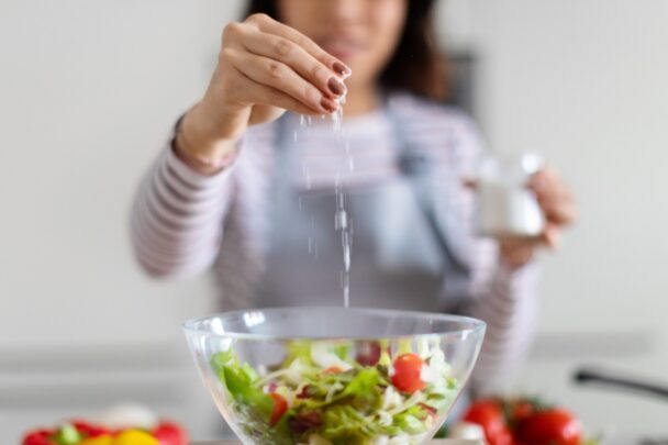 Vrouw voegt zout toe aan een schaal met salade.