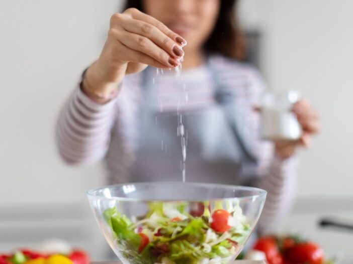 Vrouw voegt zout toe aan een schaal met salade.