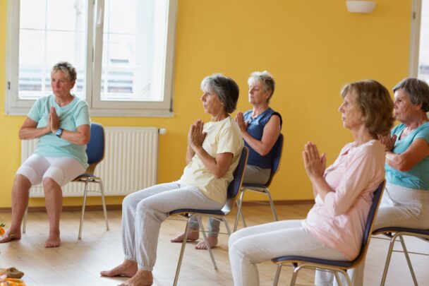 Groepje oudere vrouwen doet aan stoelyoga.