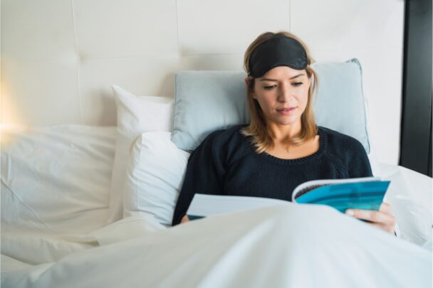 Vrouw ligt in bed een boek te lezen.