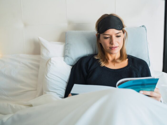 Vrouw ligt in bed een boek te lezen.