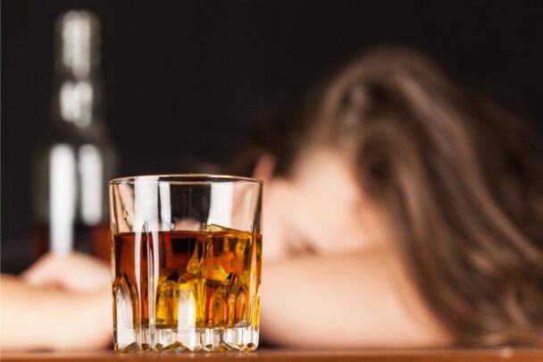 Vrouw ligt met haar hoofd op tafel. Voor haar staat een glas sterke drank.