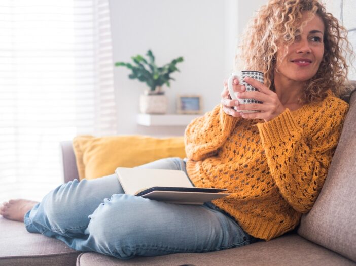 Vrouw zit ontspannen op de bank met een kopje thee.