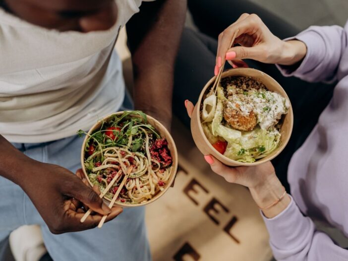 Bovenaanzicht van een man en vrouw die samen een gezonde salade met noedels eten.