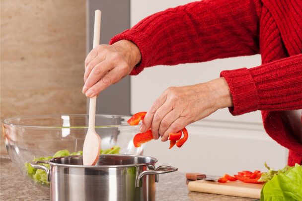 De handen van iemand die een maaltijd met rode paprika aan het bereiden is.