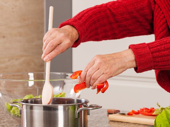 De handen van iemand die een maaltijd met rode paprika aan het bereiden is.